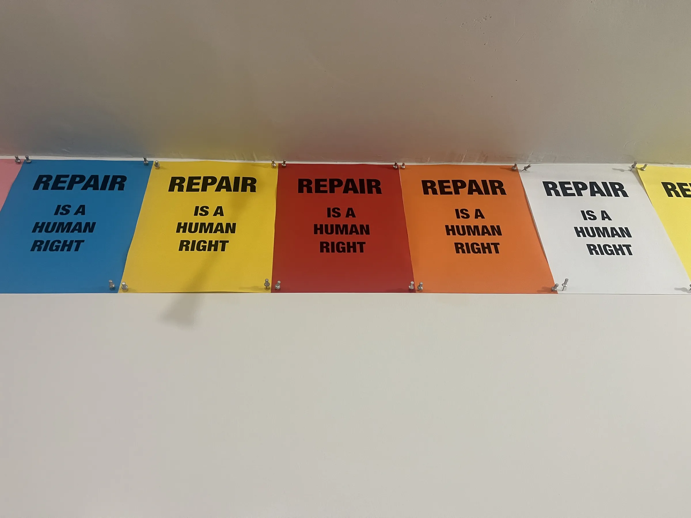 Colorful posters reading 'Repair is a Human Right' pinned to a wall in blue, yellow, red, orange, and white